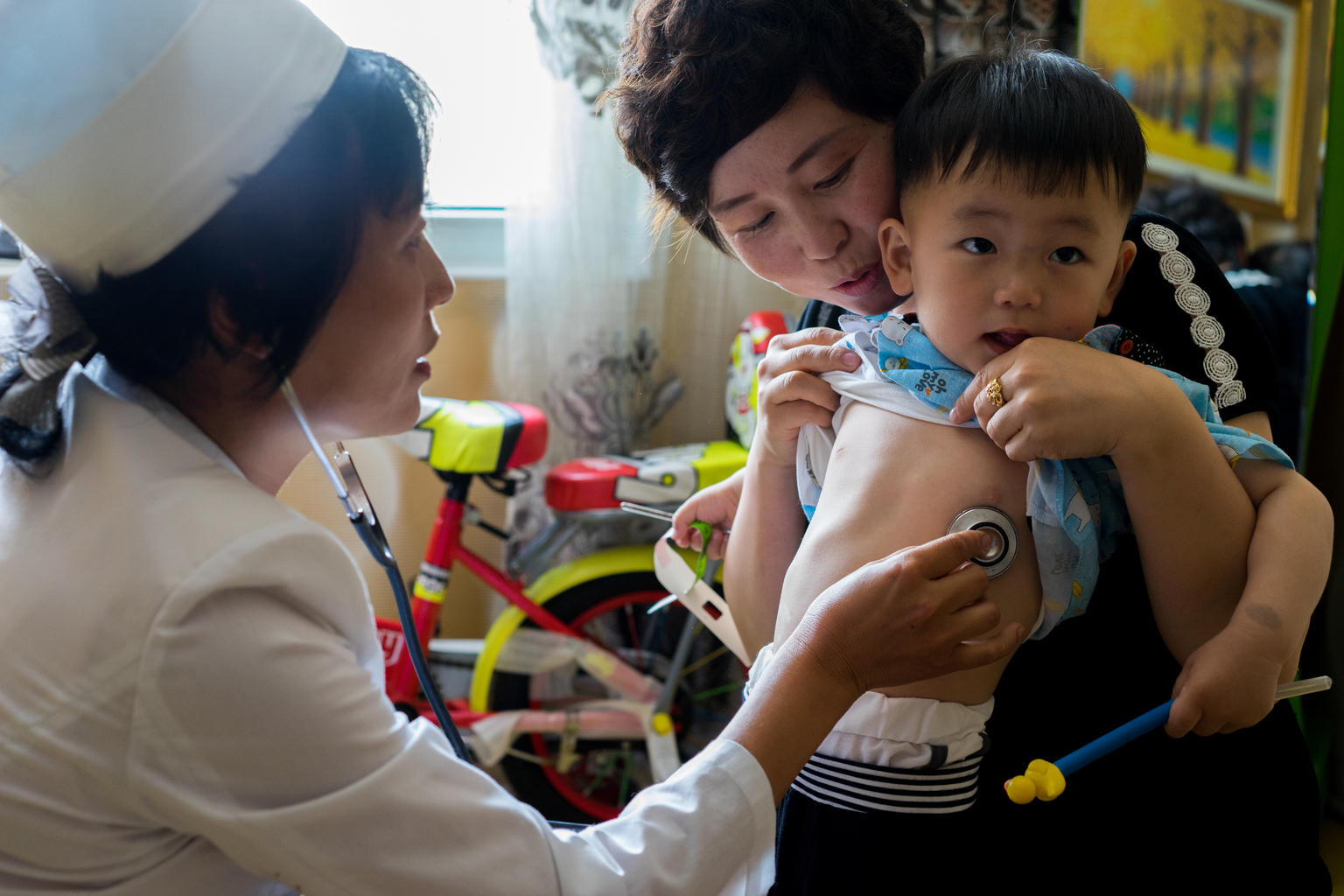 Dr Ju Song Hui, a household doctor in Jongju City, DPR Korea, checks on the health of two year old Jang Hun with his mother Pae Hye Sim. Dr Su Song Hui is using UNICEF's Household Doctors’ Bag, which is filled with essential medicines and equipment to help doctors quickly diagnose and treat patients on the spot.