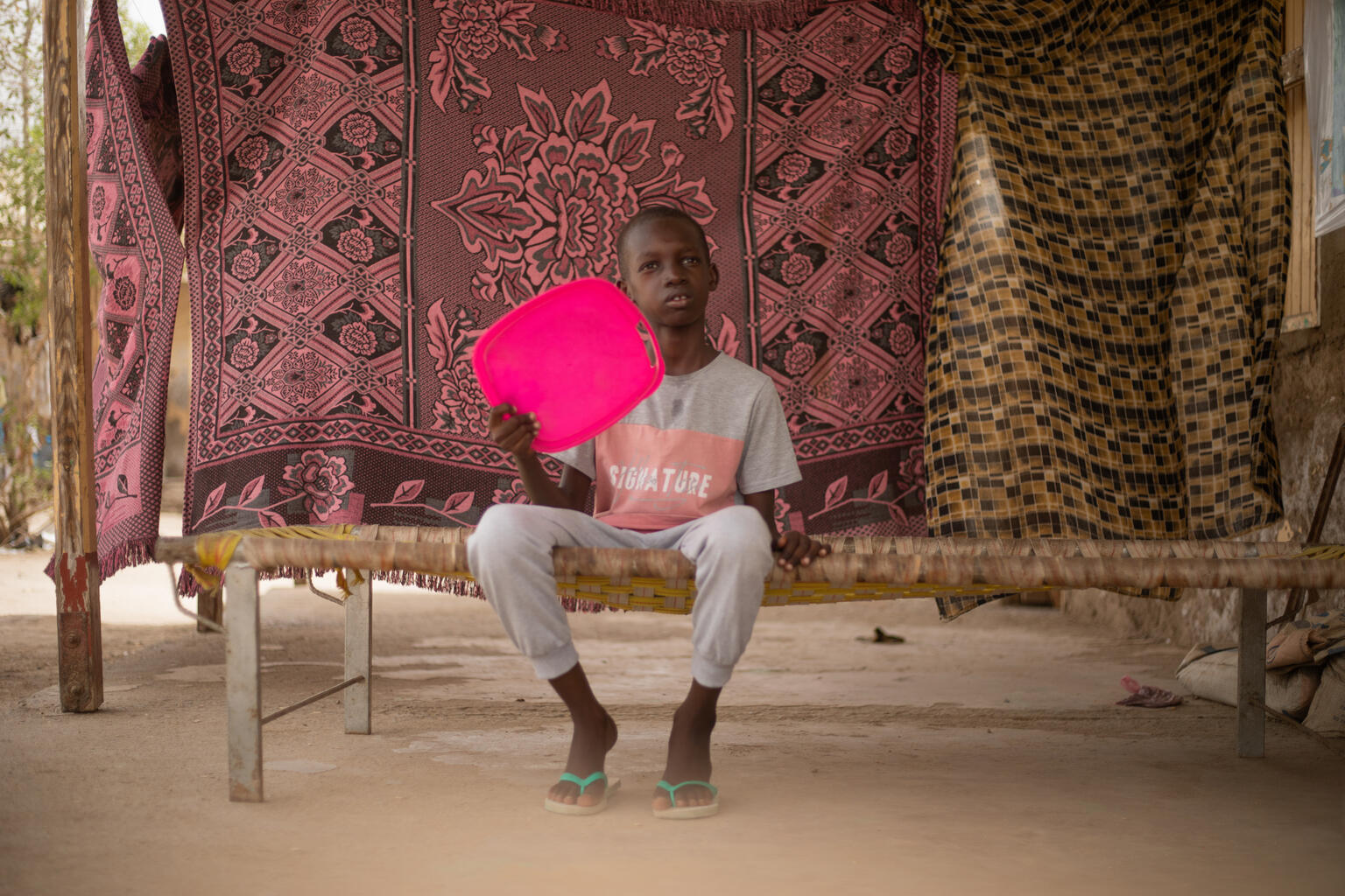 Ali, 10 years, sits under a roof and uses a plastic box lid to fan himself to cool down. In 2024, global temperatures have soared to unprecedented levels, causing a severe heatwave that is affecting millions of children in Sudan, especially those in vulnerable circumstances.